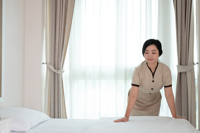 Young beautiful Asia maid arranging blanket on the bed in hotel room